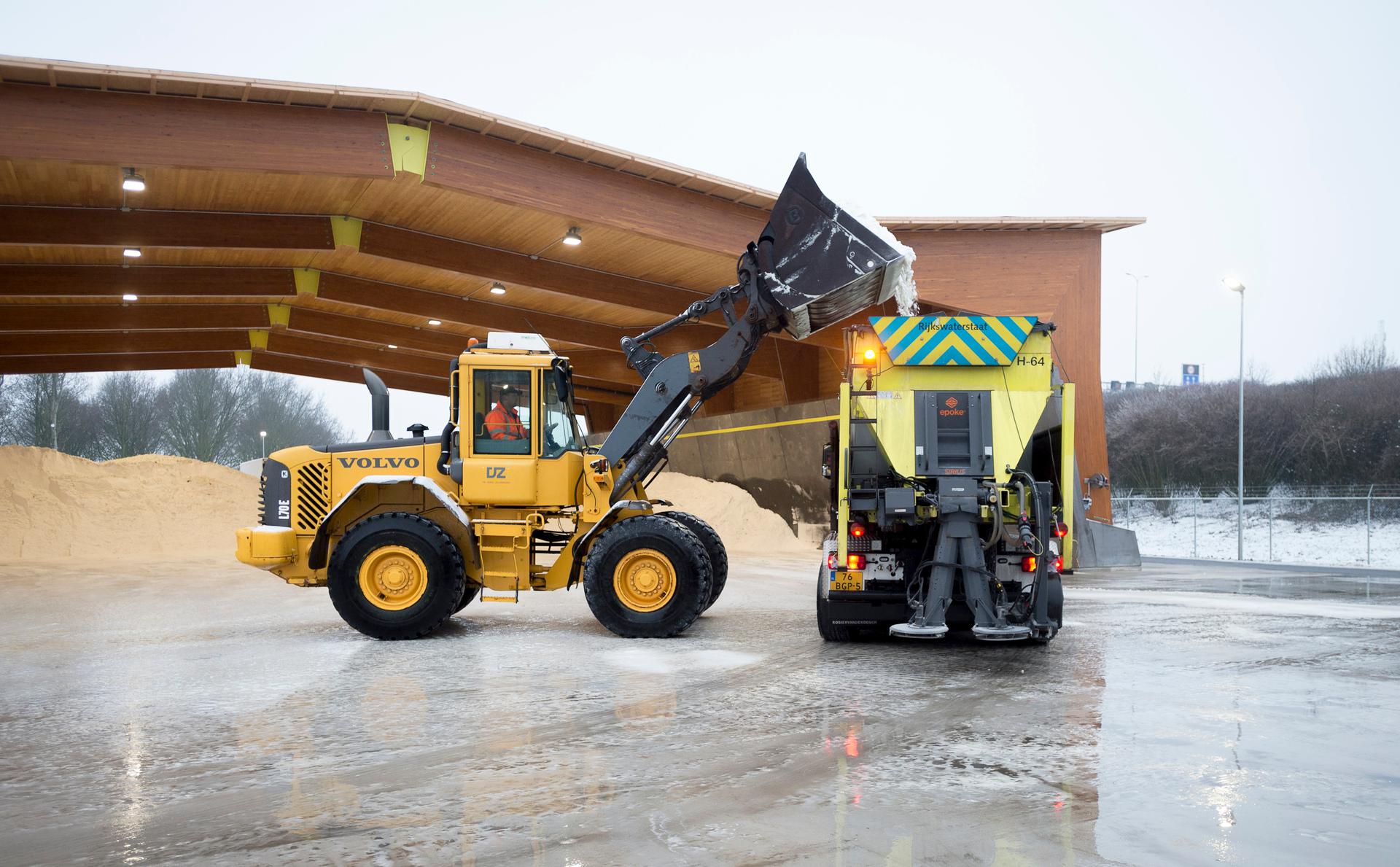 Strooiwagen wordt gevuld met zout door een graafmachine