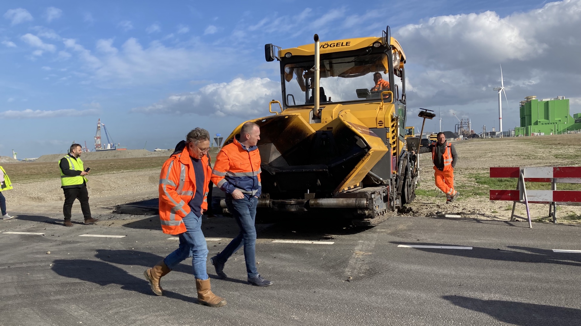 Een biobased asfalt proefvlak met een asfalteer machine en mensen in fluoriserende werkkleding