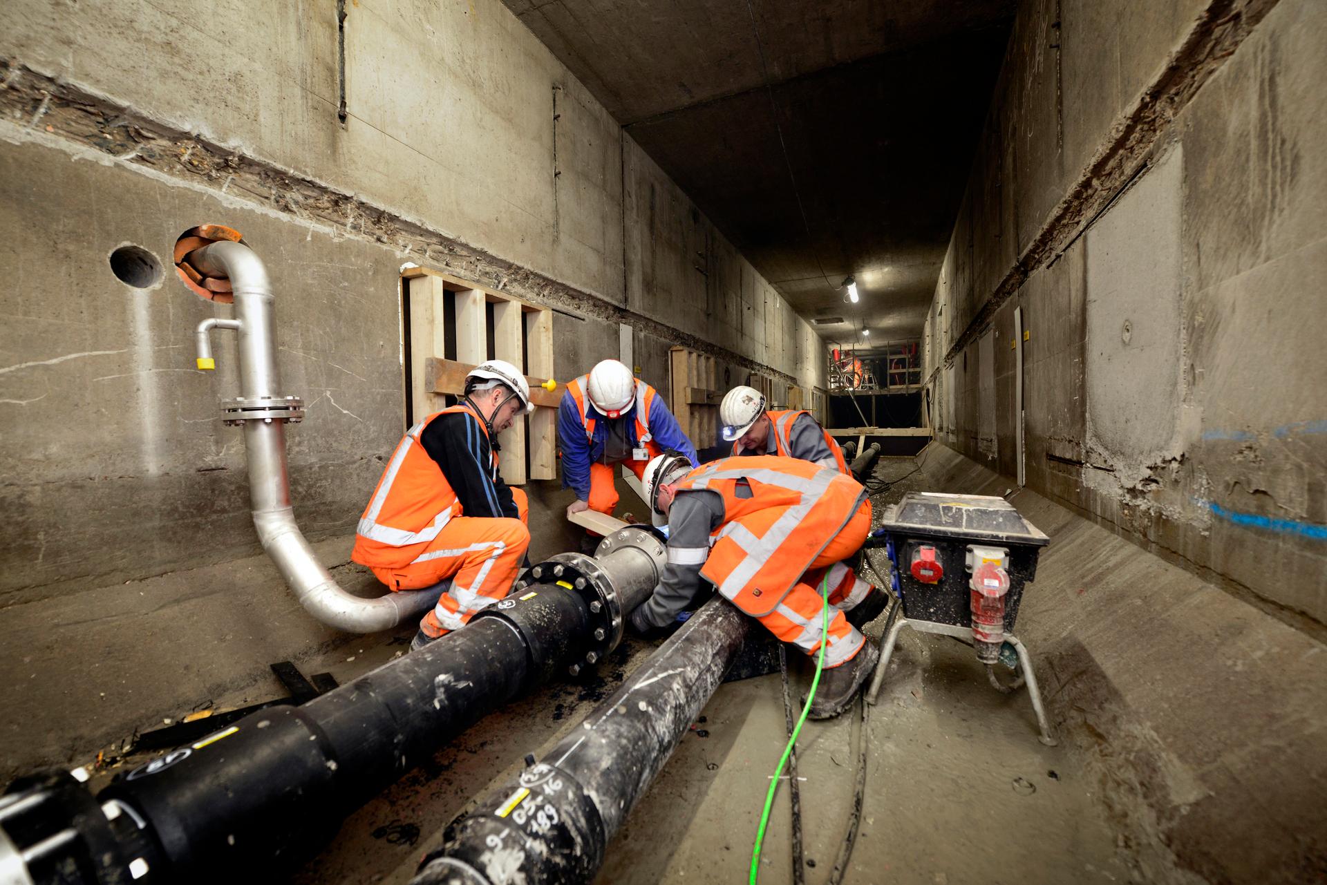 Inspecteurs van Rijkswaterstaat met oranje hesjes en helmen inspecteren buizen.