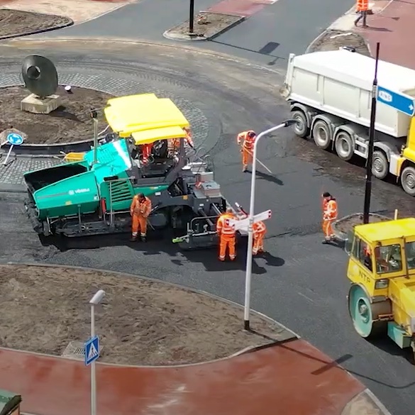 Betonroller, asfalteermachine en kiepwagen werken aan het grasfalt op een rotonde